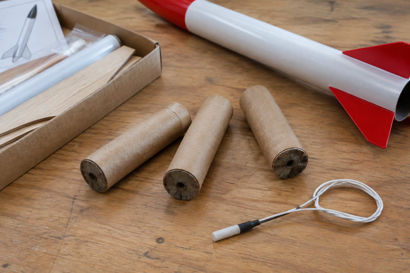 Three unbranded model rocket engines beside an assembled model rocket kit and an igniter on a wooden workbench