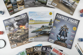 Assorted model making magazines including Military Modelcraft, Scale Aircraft, and Fantasy Figure International on a white table, seen at MPM Hobbies.