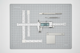 Precision measuring tools and cutting mats for scale modeling including rulers, calipers, and machinist squares on professional work surface