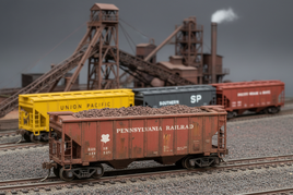 HO scale model train hopper cars on tracks with industrial backdrop, model railroad hobby scene