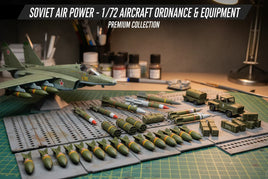 1/72 scale Soviet aircraft model with ordnance, equipment, trucks, and crates on a hobby workbench