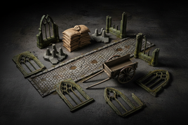 Assortment of 1/35 scale diorama accessories including sandbags, barricades, cobblestone road sections, a wooden farmer's cart, and gothic stone building pieces arranged on a dark textured surface for scale model diorama building
