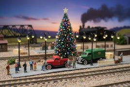 Miniature Christmas village scene with model train, holiday tree, and vintage vehicles at sunset
