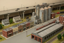 Realistic HO scale model train layout with industrial buildings, town storefronts, and overpass, from MPM Hobbies 3D printed collection.