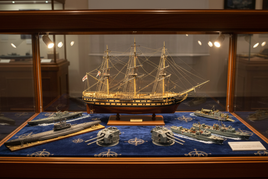 Detailed ship and submarine model kits in a glass display case, perfect for hobby enthusiasts at MPM Hobbies