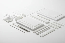 Model building supplies kit with white plastic sheets, rods, and hobby knife on clean background