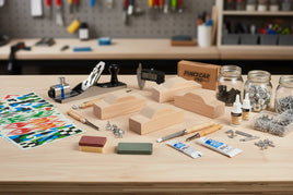 Pine car racing kit with wood blocks, tools, decals, wheels, and hardware on workshop table at MPM Hobbies.