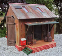 Model of a rustic shed with wooden walls, metal roof, and brick foundation on a gravel surface.