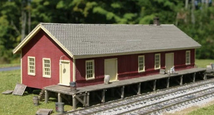 Model train station building on tracks with a forest background