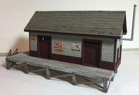 Model of a small building with a platform in front on a plain background