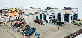 Model of a vintage car dealership with miniature cars and people around.