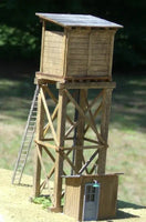 Wooden lookout tower with a smaller structure at its base on a grassy background