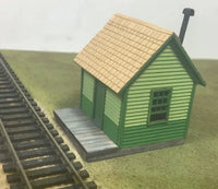 Model train station building next to railway tracks on a grassy field