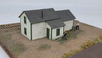 Model of a small building with green doors and gray roof on a plain background