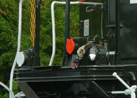 Close-up of a black mechanical component with a red light and white railings in an outdoor setting.