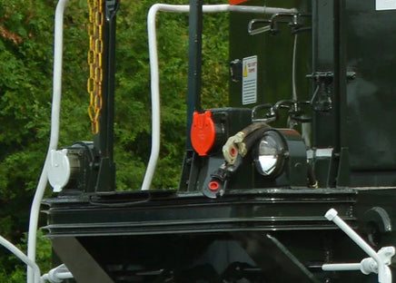 Close-up of a black mechanical component with a red light and white railings in an outdoor setting.