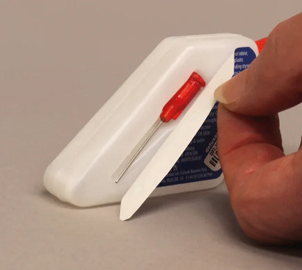Hand holding a white plastic tool with a red screwdriver-like component on a beige background