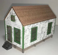 Model of a small house with white walls, green windows, and brown roof on a gray background