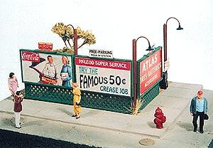 Model of a vintage gas station with people and signs, featuring a Coca-Cola sign.