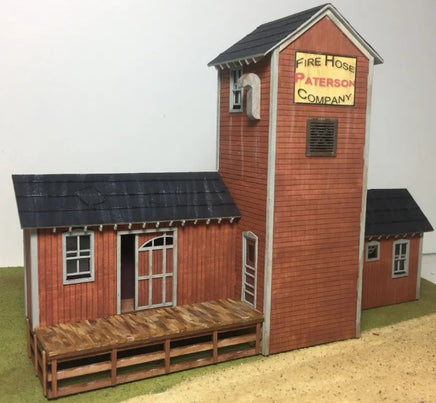 Model of a fire station with a tall tower and smaller building, featuring a sign for 'Fire Hose Paterson Company'.