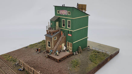 Model of a two-story building with green facade and wooden accents on a white background