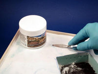 Person applying modeling clay to a surface with a tool, next to a container of modeling clay on a blue background.