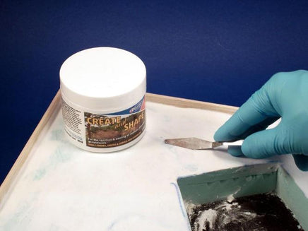 Person applying modeling clay to a surface with a tool, next to a container of modeling clay on a blue background.