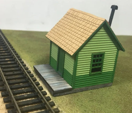 Model train station building next to railway tracks on a grassy surface