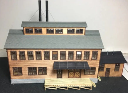 Model of a building with a gray roof and wooden exterior on a dark surface.
