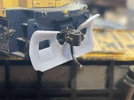 Close-up of a model train engine with a white front scoop and detailed components.