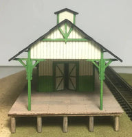 Model train station with green roof and white walls on a gray background