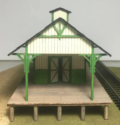 Model train station with green roof and white walls on a gray background