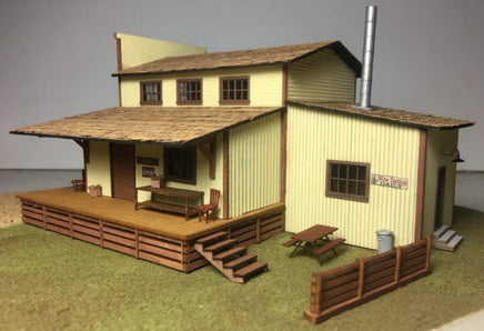 Model of a rustic two-story building with a wooden deck and picnic table.