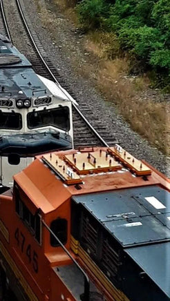 Two trains on a railway track with one orange and black train partially off the tracks.
