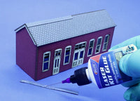 Model building kit with a small house model, glue bottle, and tools on a blue background