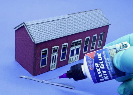 Model building kit with a small house model, glue bottle, and tools on a blue background
