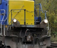 Close-up of a train engine with a yellow front and blue sides, moving on tracks with greenery in the background.