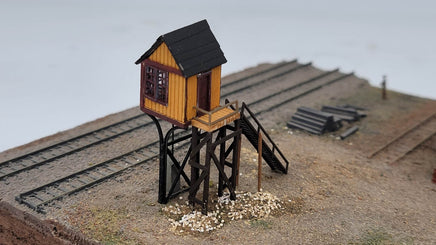 Model of a small wooden cabin on stilts with tracks in the background