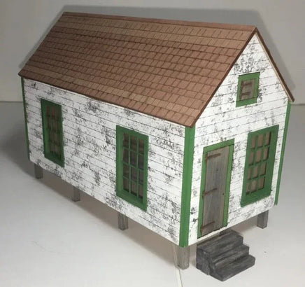 Model of a small house with a brown roof and green trim on a white background