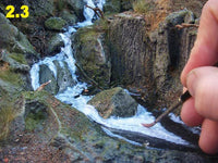Hand holding a small tool near a miniature waterfall and rocks