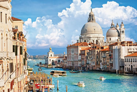 Venice cityscape with Grand Canal, boats, and historic buildings under a blue sky with clouds.