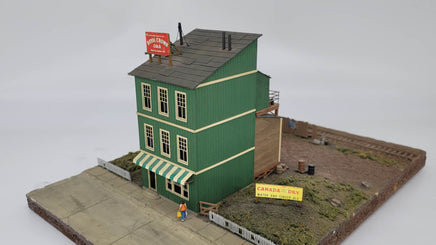 Model of a two-story building with green facade and red sign on a white background