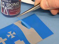 Person applying blue tape to a surface with a can of 'Opaques Masking Magic' in the background.