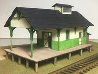 Model train station with green and brown colors on a plain background
