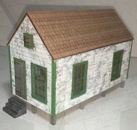 Model of a small house with a brown roof and green windows on a white floor.
