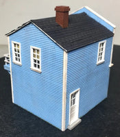 Model of a blue house with a black roof and red chimney on a dark surface.