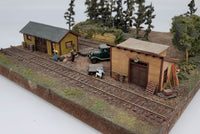 Model train setup with wooden buildings and people near a railway track.