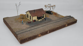 Model train layout with a small building, trees, and a car on a plain background
