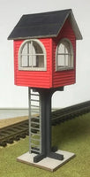 Model train signal tower with red body, black roof, and white base on a track.