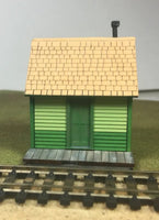 Model train station building with green base and beige roof on a track